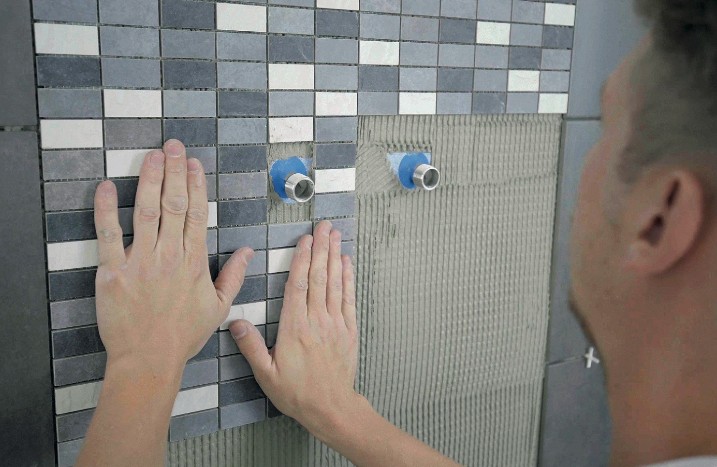 Mosaikmatten werden mit Aussparungen um Wasseranschlüsse an der Wand gelegt.